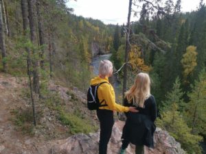 Kaksi henkilö seisovat kallion reunalla metsässä