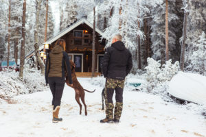 Mies, nainen ja koira talon pihamaallatalvisissa maisemissa