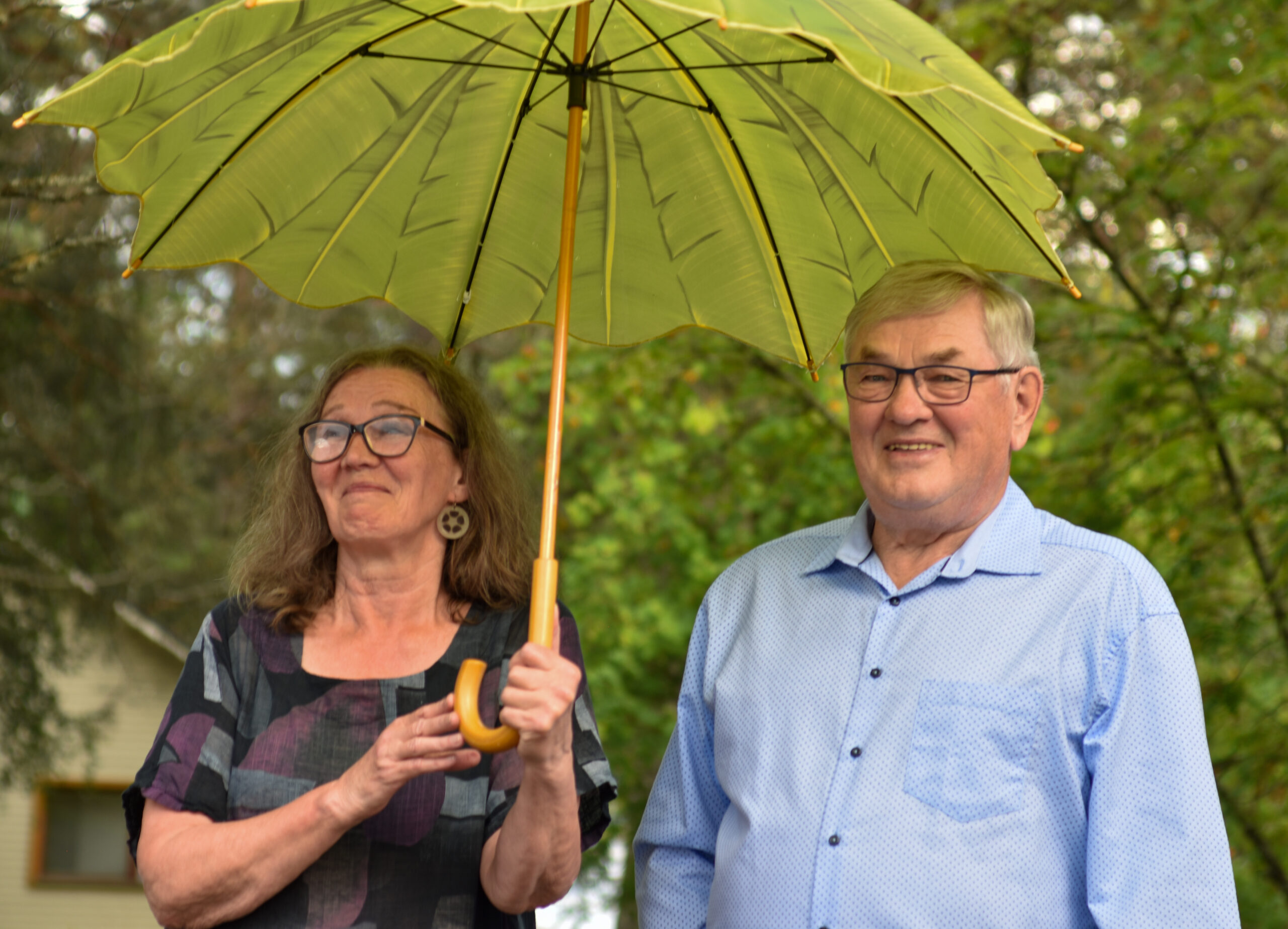 Kaksi henkilöä hymyilee sateenvarjon alla